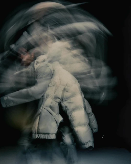 Abstract motion blur of a person wearing a puffer jacket against a dark background, creating an ethereal and dynamic visual effect.