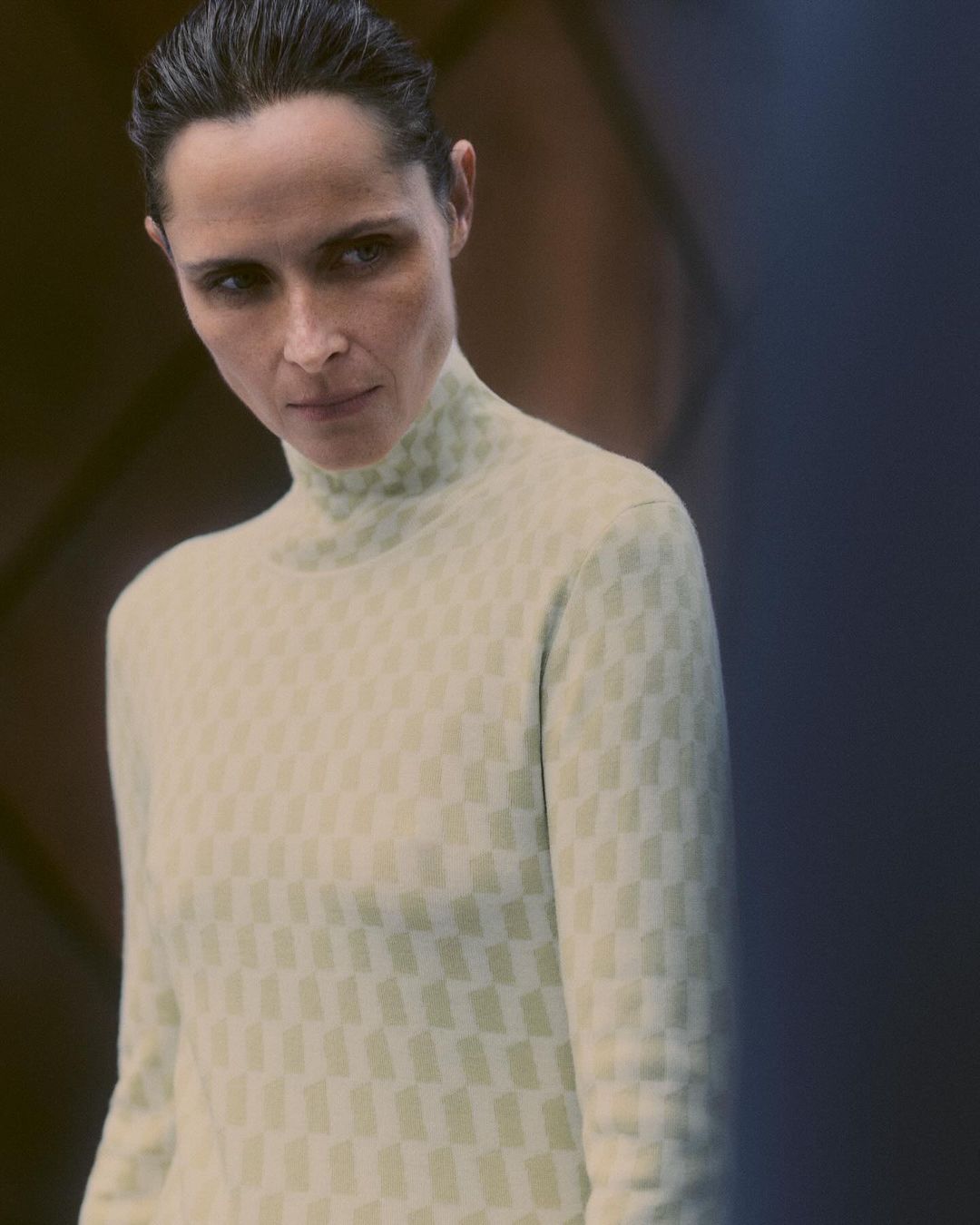 Woman in patterned turtleneck sweater poses indoors with soft, directional lighting on her face and dark hair.