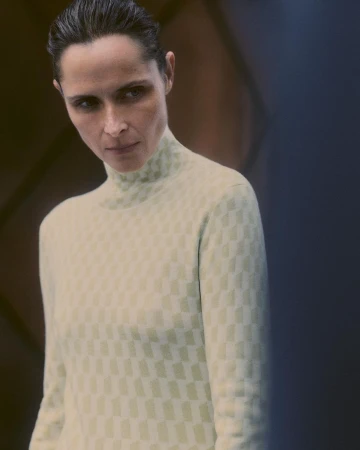 Woman in patterned turtleneck sweater poses indoors with soft, directional lighting on her face and dark hair.