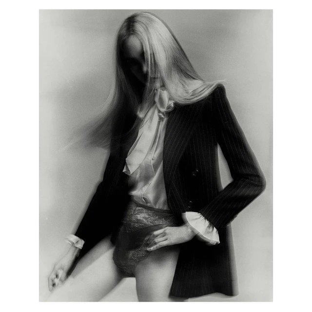 Monochrome portrait of a woman in a pinstripe blazer, blouse, and lace underwear against a simple light gray backdrop, capturing a minimalist fashion aesthetic.