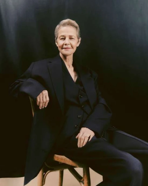 Elegant senior woman in tailored suit posing on wood chair against dark backdrop in a portrait shot, studio lighting