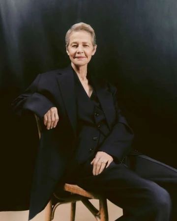 Elegant senior woman in tailored suit posing on wood chair against dark backdrop in a portrait shot, studio lighting