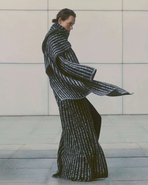 Fashion shot of a model in a black and silver striped dress with a high neck, posing in an indoor setting with natural light.
