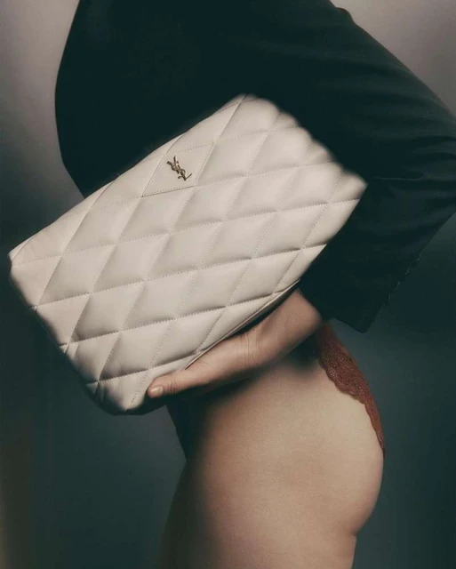 Close-up studio shot featuring a cream-colored, quilted Saint Laurent clutch purse held by a fair-skinned woman wearing black and red clothing.