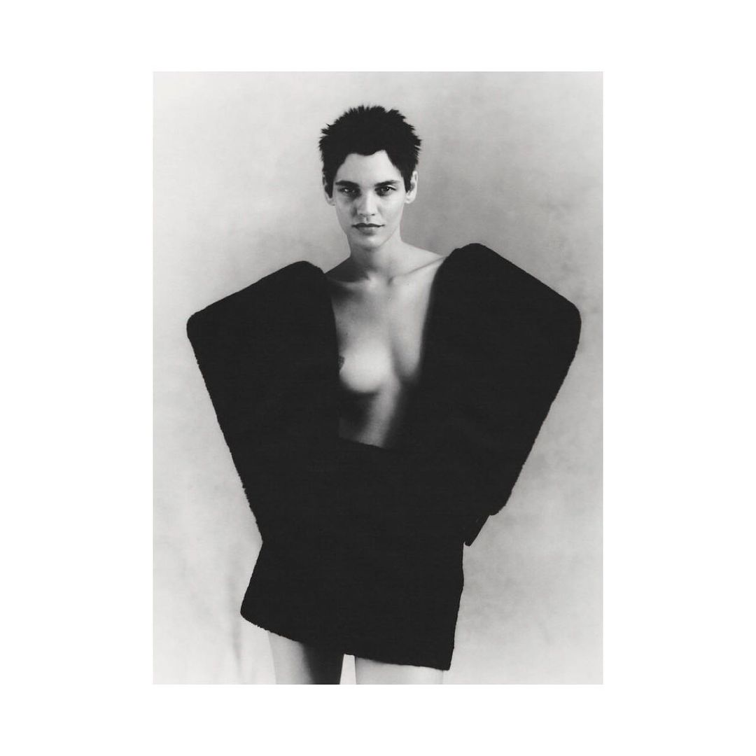 Monochrome portrait of a female fashion model with short dark hair wearing an oversized black jacket against a plain background.
