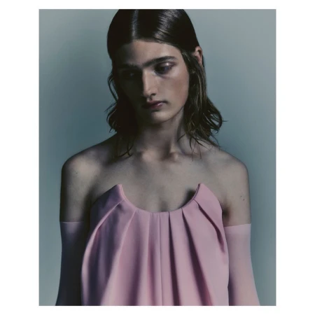 Portrait of a model with long dark hair wearing a pink strapless top against a neutral grey studio background.