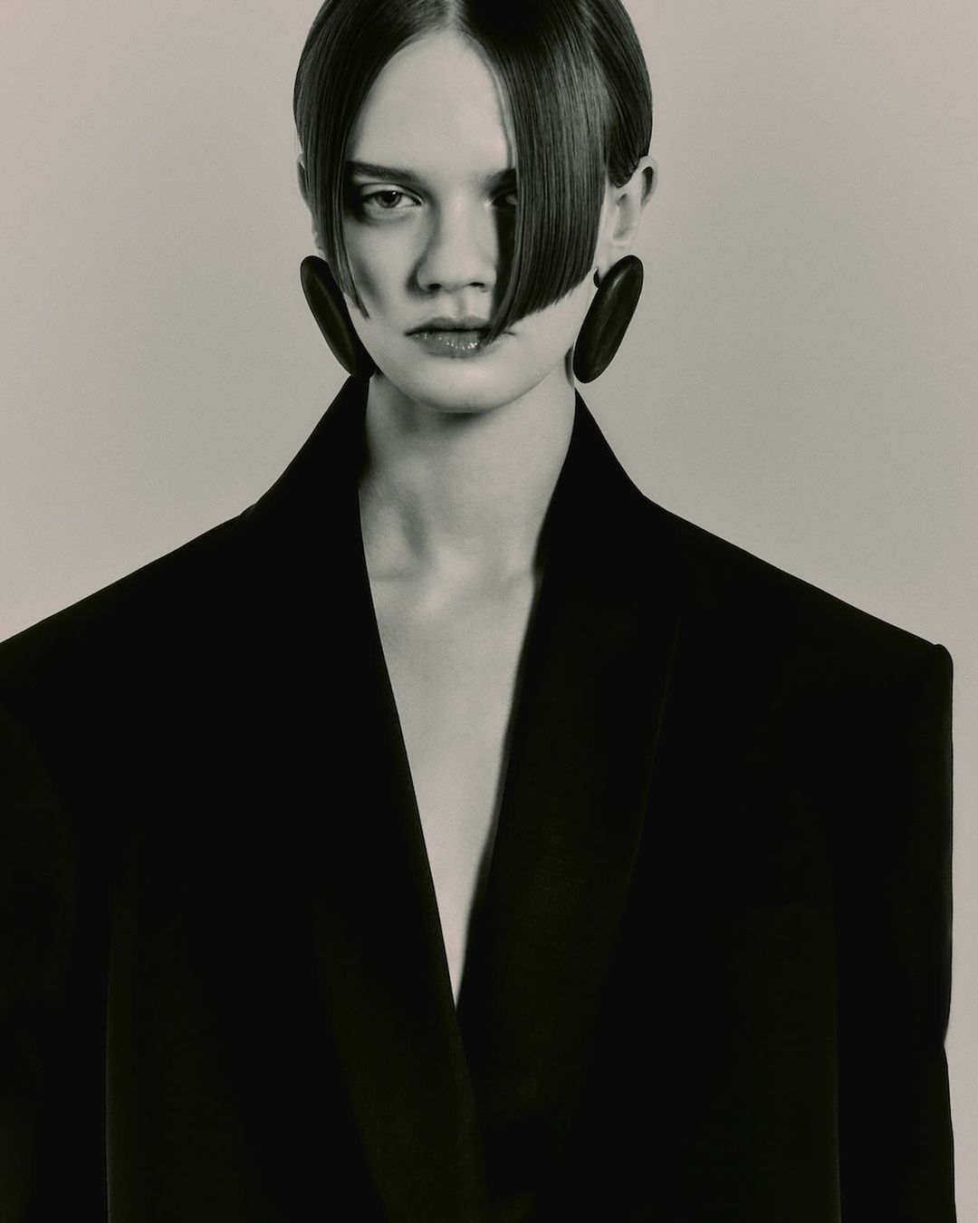Close-up portrait of a model with sleek dark hair wearing a structured black blazer and large oval earrings by photographer Darren Gwynn