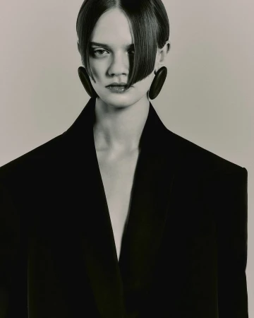 Close-up portrait of a model with sleek dark hair wearing a structured black blazer and large oval earrings by photographer Darren Gwynn