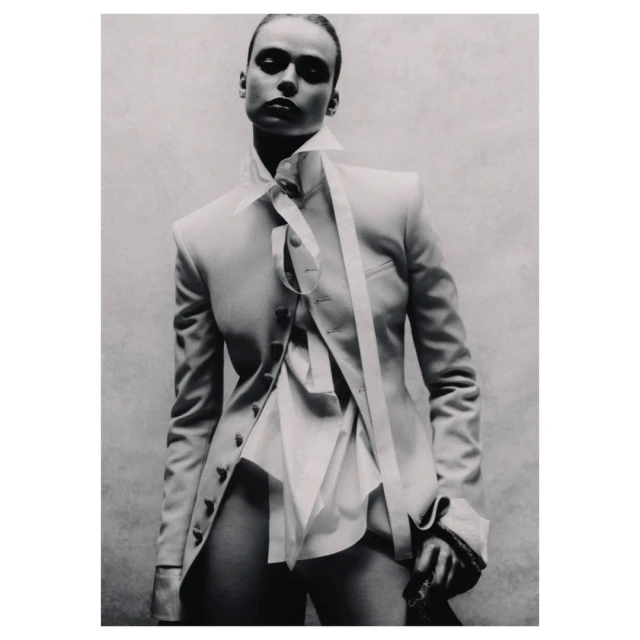 Monochrome studio shot of a young adult fashion model in a blazer and dress shirt, posing with dramatic lighting against a neutral backdrop.