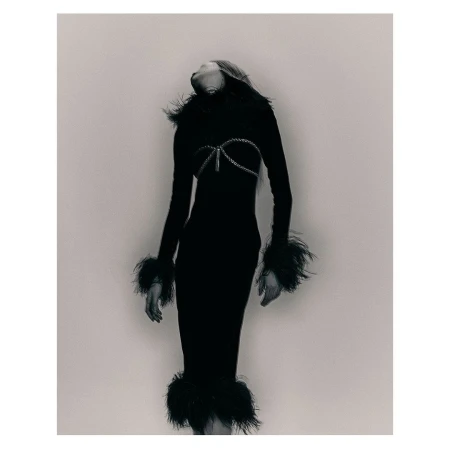 Monochrome fashion shot of a woman in a form-fitting black dress with feather trim, posing with her head tilted back in a studio.