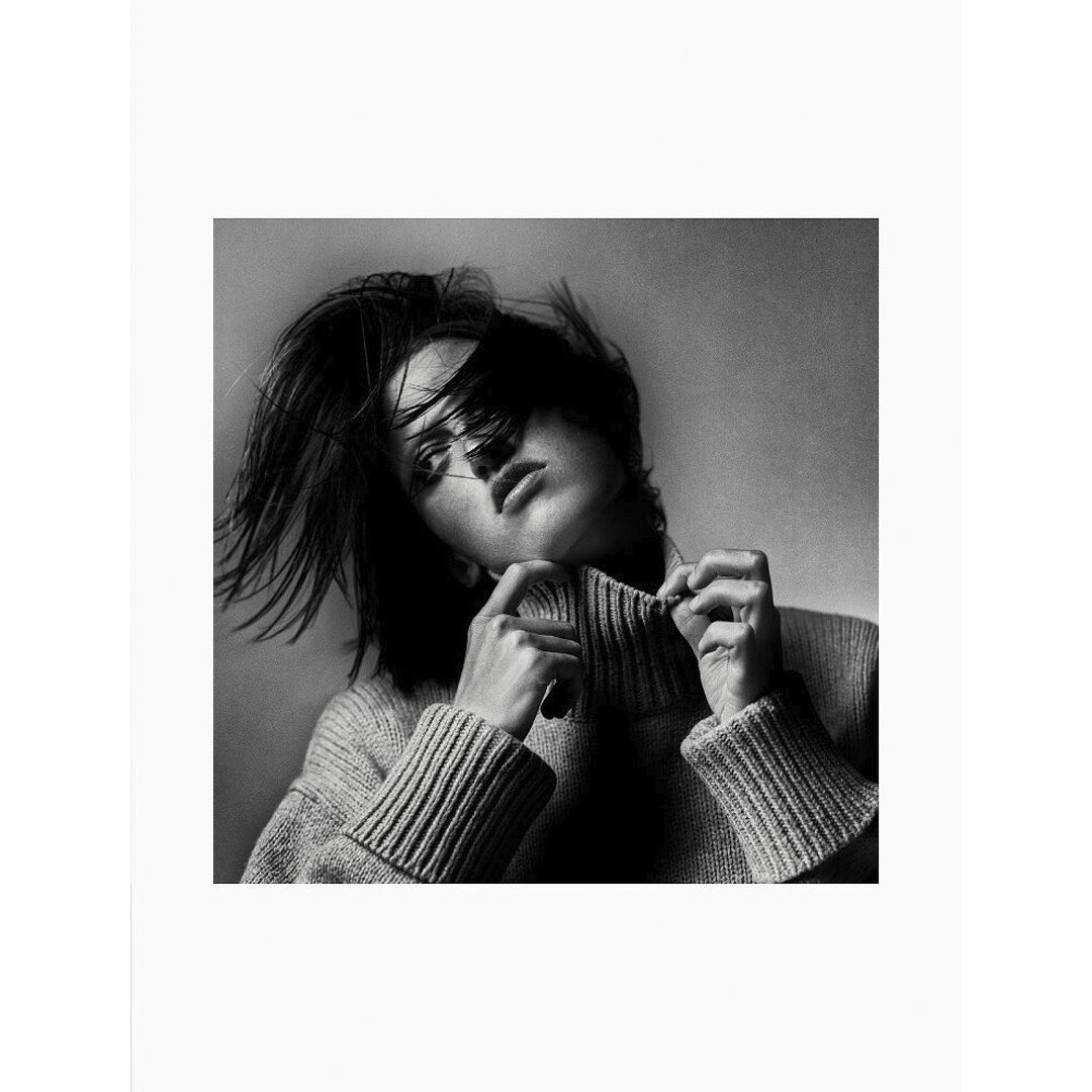 Black and white portrait of a woman wearing a ribbed turtleneck sweater, pulling at the collar in London