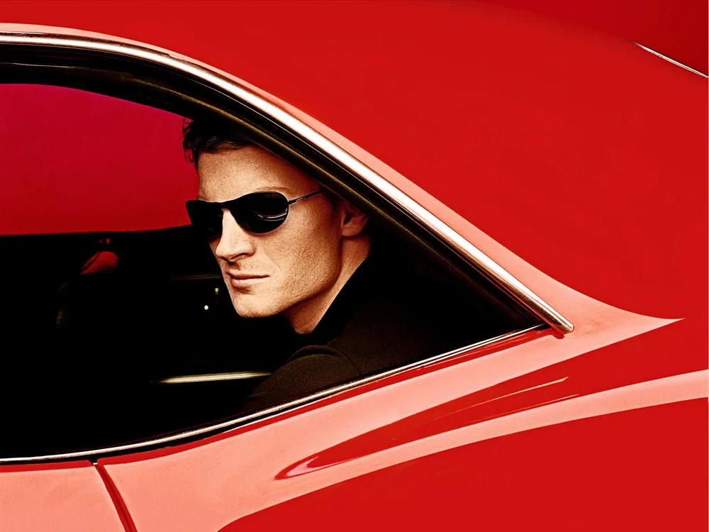 Stylish adult male with sunglasses sits in a classic red car, side view. Automotive and fashion concept. Bright, saturated color palette.