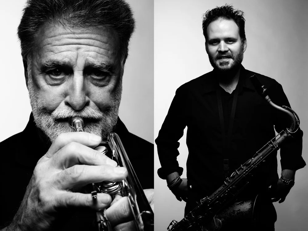 Black and white portrait of two adult musicians playing a trumpet and saxophone indoors against a gradient background.