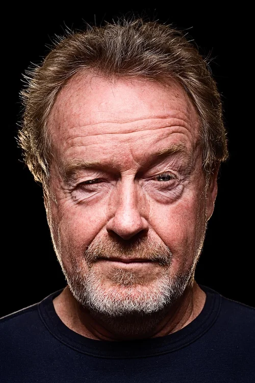 Close-up portrait of an adult male with graying hair and a beard, wearing a dark shirt, set against a stark black background.