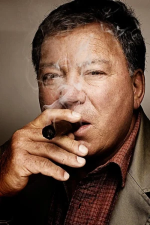 Close-up portrait of William Shatner smoking a lit cigar with swirls of white smoke drifting past his face.