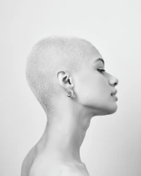 Profile portrait of a person with a buzzcut and hoop earring against a plain light background