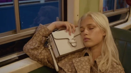 Blonde woman sleeping against a structured white handbag inside a transit vehicle with dark windows