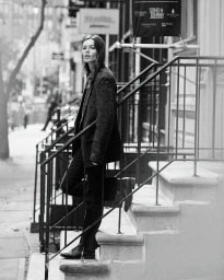 Monochrome portrait of a model leaning on stone stoop stairs wearing a plaid blazer and dark trousers in New York.