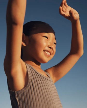 Young child with arms raised smiling against a clear blue sky background