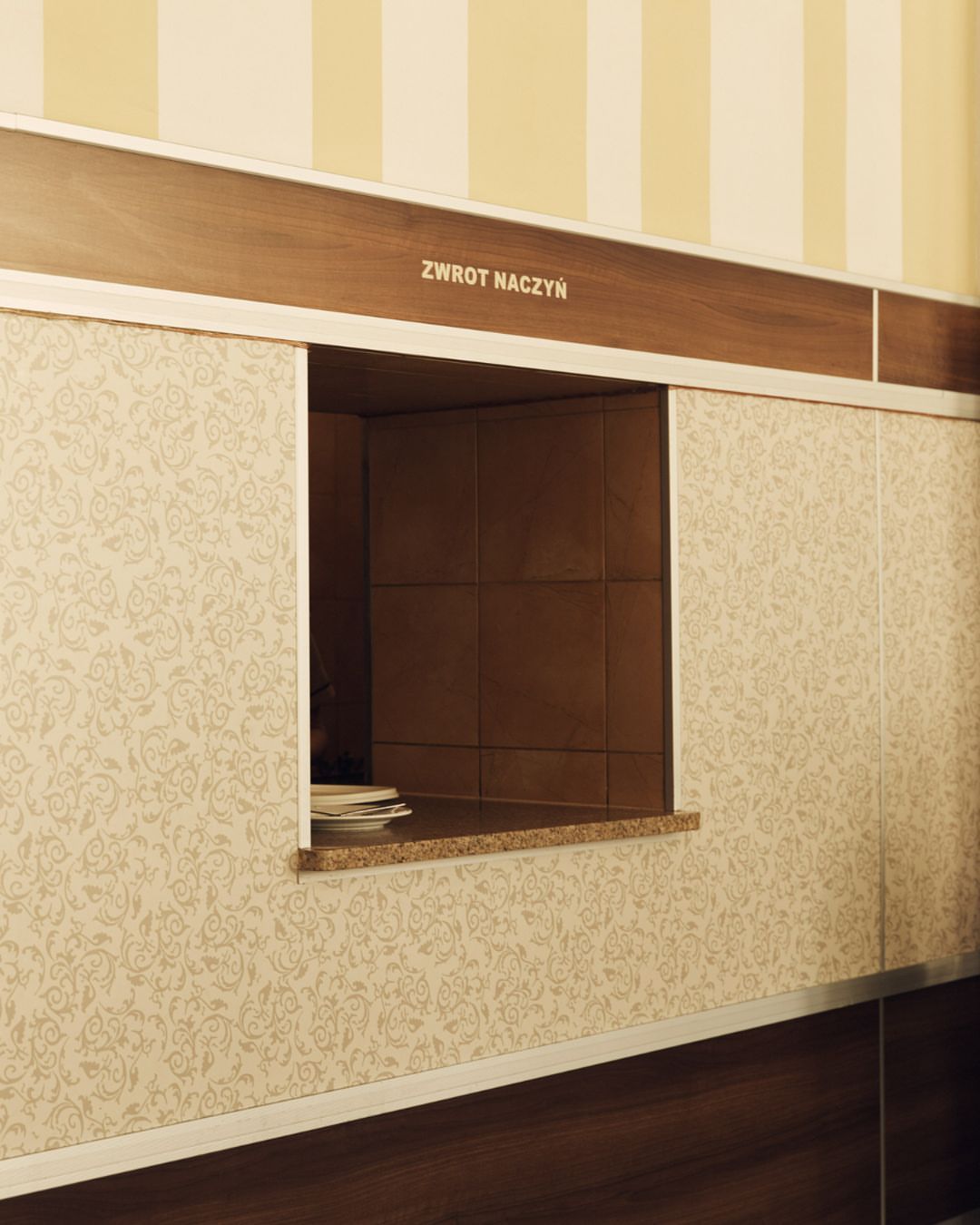 Empty dish return window with a patterned wall in a restaurant setting, providing a glimpse into the dining space.