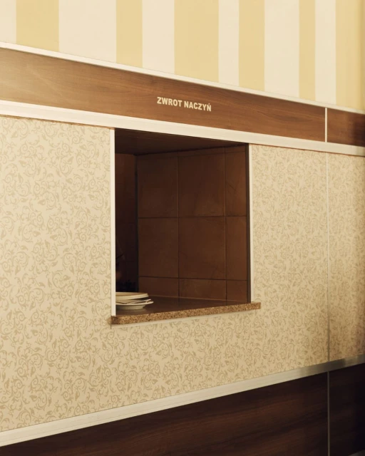 Empty dish return window with a patterned wall in a restaurant setting, providing a glimpse into the dining space.