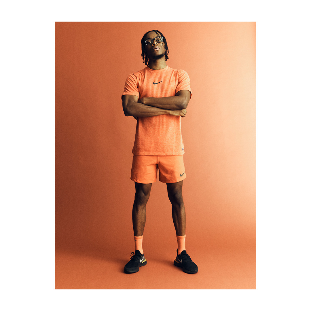 Athletic man in orange sportswear posing in studio. Male fashion model wearing matching Nike shirt and shorts. Youthful sports fashion.