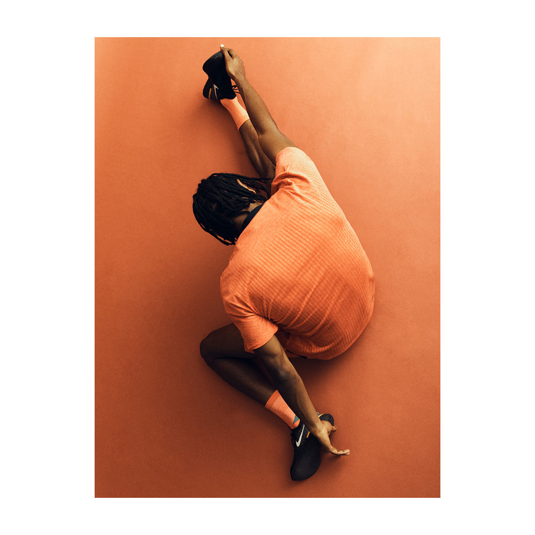 Person in athletic wear strikes a unique pose against an orange background, showcasing flexibility and strength in a minimalist studio setting.