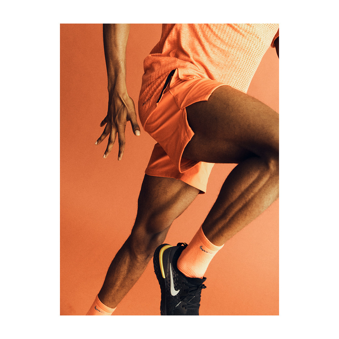 Athletic man running in studio. Athlete in orange athletic wear and black running shoes in motion against an orange backdrop.