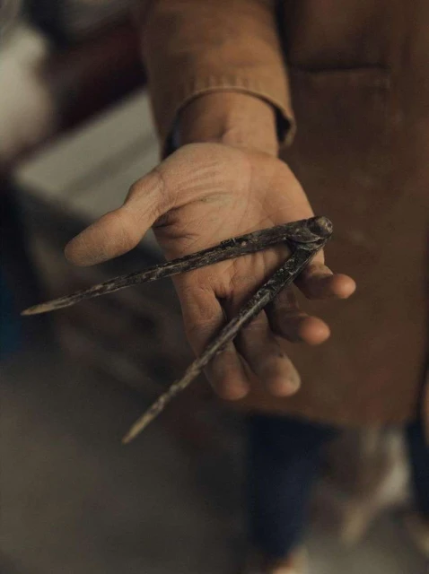 Close-up of an adult hand holding a set of rusty metal calipers, with tan clothing visible and a blurred background. 