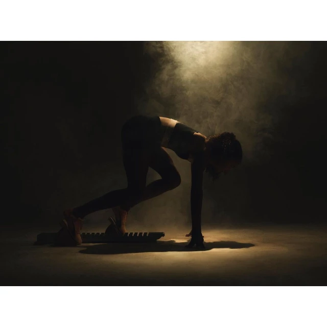 Female athlete in dark sportswear poses on a sled fitness board amidst smoky, moody lighting in a fitness setting.