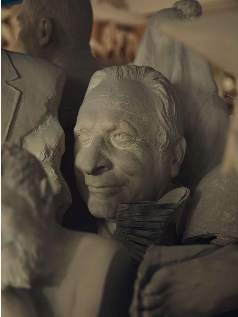 Gray-toned sculptures of human faces, shoulders, and hands are densely packed together, creating a textured, monochromatic visual display.