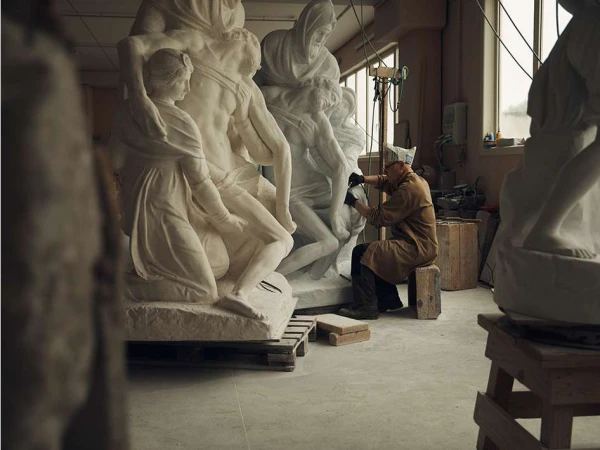 Sculptor working on a large marble sculpture in a studio, shaping the stone with hand tools, in a workspace with other sculptures.