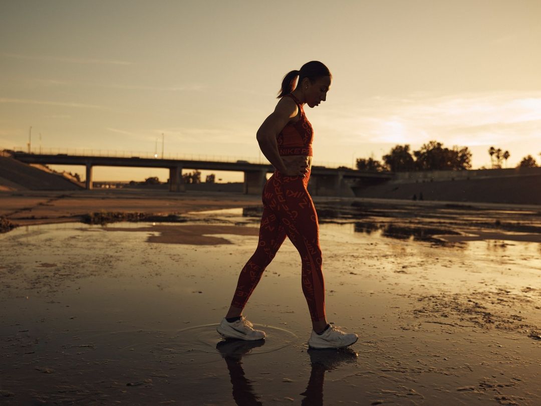 Athletic woman in activewear exercising outdoors near a bridge during golden hour, showcasing fitness and healthy lifestyle.