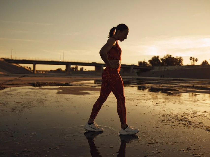 Athletic woman in activewear exercising outdoors near a bridge during golden hour, showcasing fitness and healthy lifestyle.