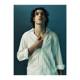 Portrait of a man with dark curly hair wearing an unbuttoned white shirt against a dark blue background.