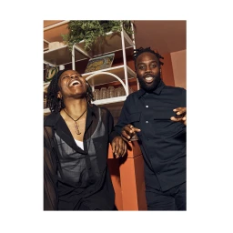 Two smiling Black individuals leaning against an orange counter inside a bar, captured by photographer Dave Imms.