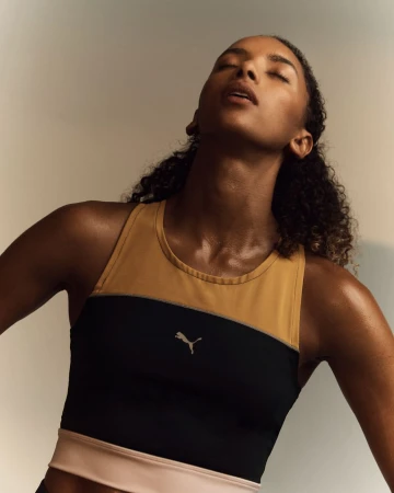 Close-up portrait of a woman wearing a mustard and black Puma sports top with her head tilted back.