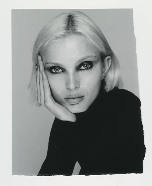 Monochrome portrait of a fair-skinned woman with platinum blonde hair in a black turtleneck sweater, gazing into the camera.