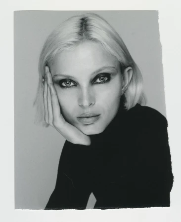 Monochrome portrait of a fair-skinned woman with platinum blonde hair in a black turtleneck sweater, gazing into the camera.