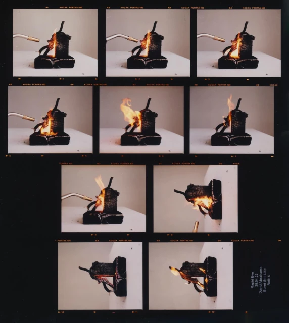 Sequence of images showing a black, geometric object being set on fire by a small blowtorch against a white background in a studio setting.