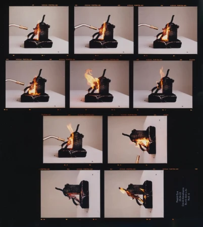Sequence of images showing a black, geometric object being set on fire by a small blowtorch against a white background in a studio setting.