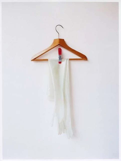 White gloves hang on a wooden hanger against a white wall, held by a red clothespin, providing a simple and elegant composition.