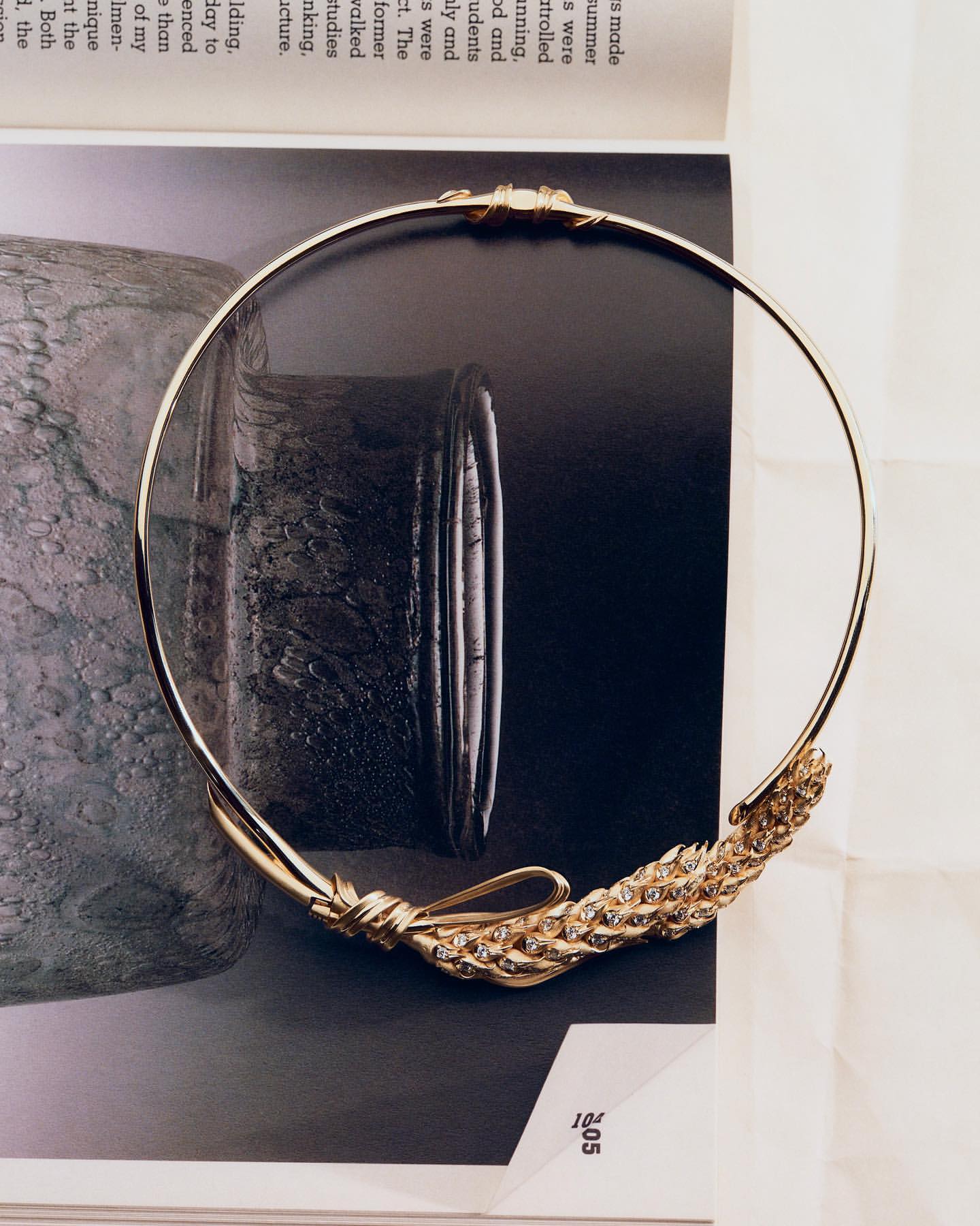 Golden neck ring jewellery with woven metal embellishment laying on the surface of a magazine page. Elegant fashion accessory.