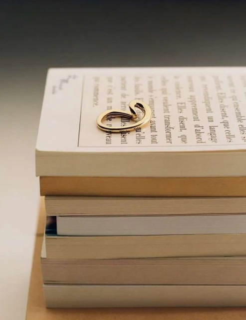 Close-up of a gold ring with a unique, looping design resting on top of a stack of books with visible text, highlighting jewelry and reading.