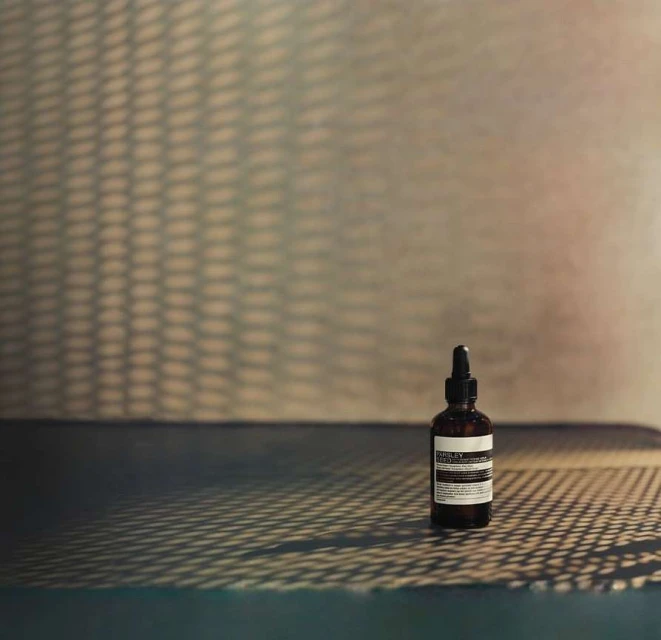 Amber glass bottle with dropper on dark surface with shadow patterns against cream-colored wall, beauty product shot.
