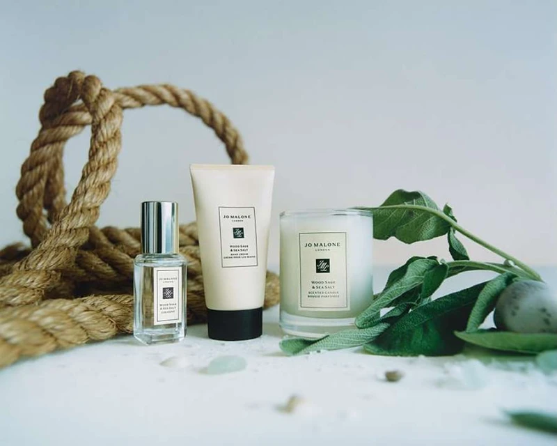 Jo Malone London fragrance, lotion, and scented candle arranged with jute rope and green leaves against a neutral background.