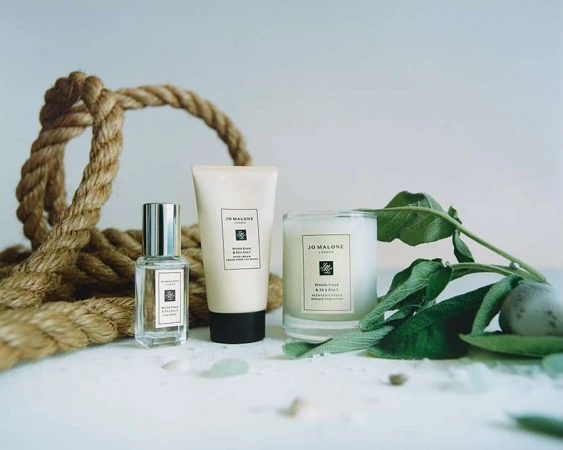 Jo Malone London fragrance, lotion, and scented candle arranged with jute rope and green leaves against a neutral background.
