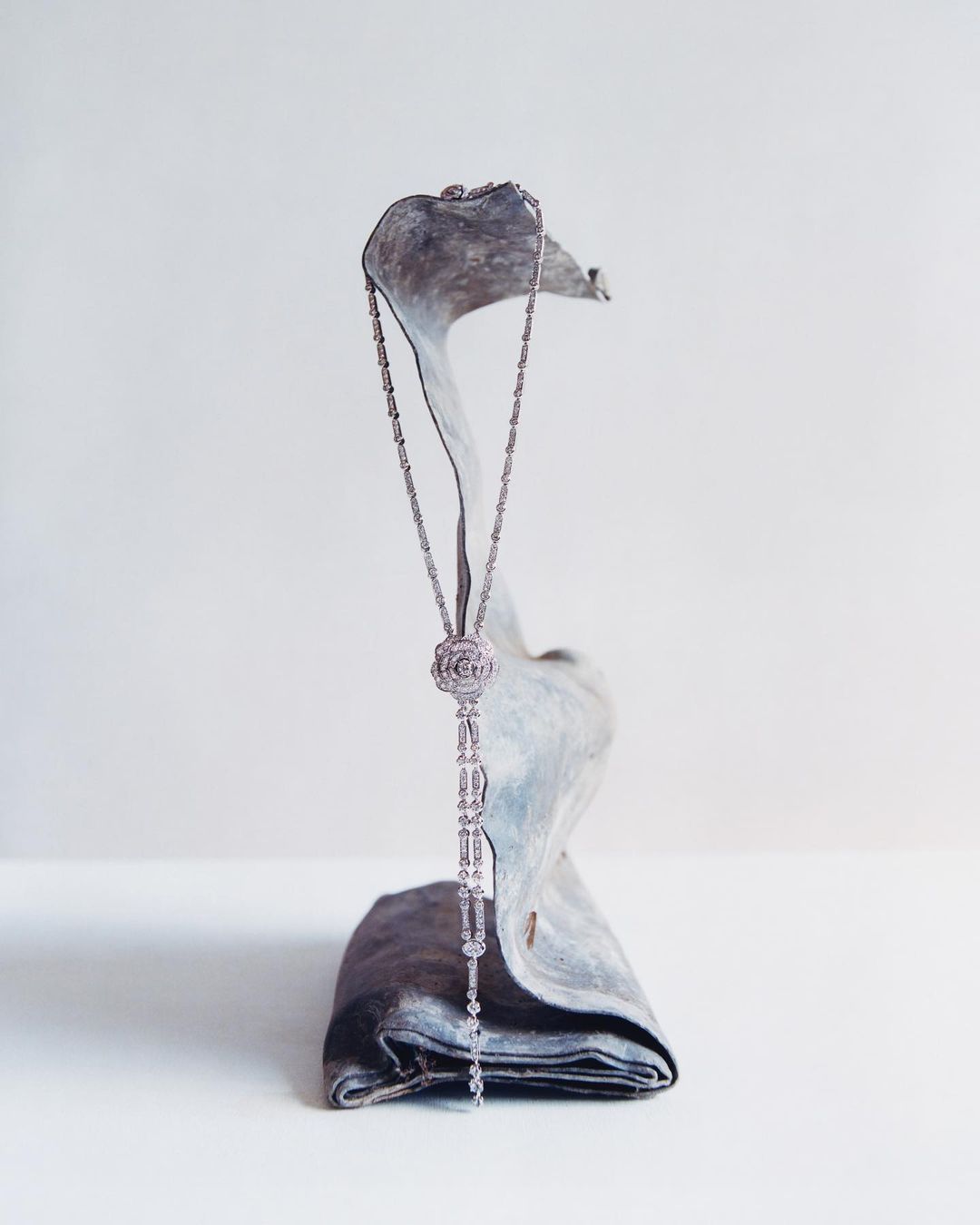 Elegant silver necklace with floral pendant rests on a draped grey fabric, showcasing jewelry craftsmanship and minimalist styling.