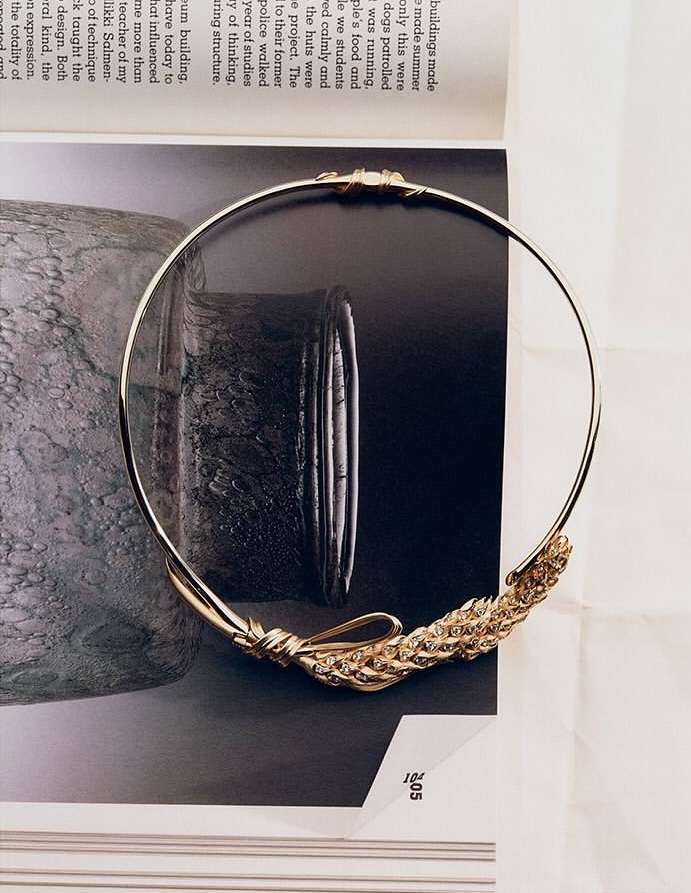 Close-up of a gold necklace with an intricate wheat design on a magazine page, showcasing fashion and jewelry.