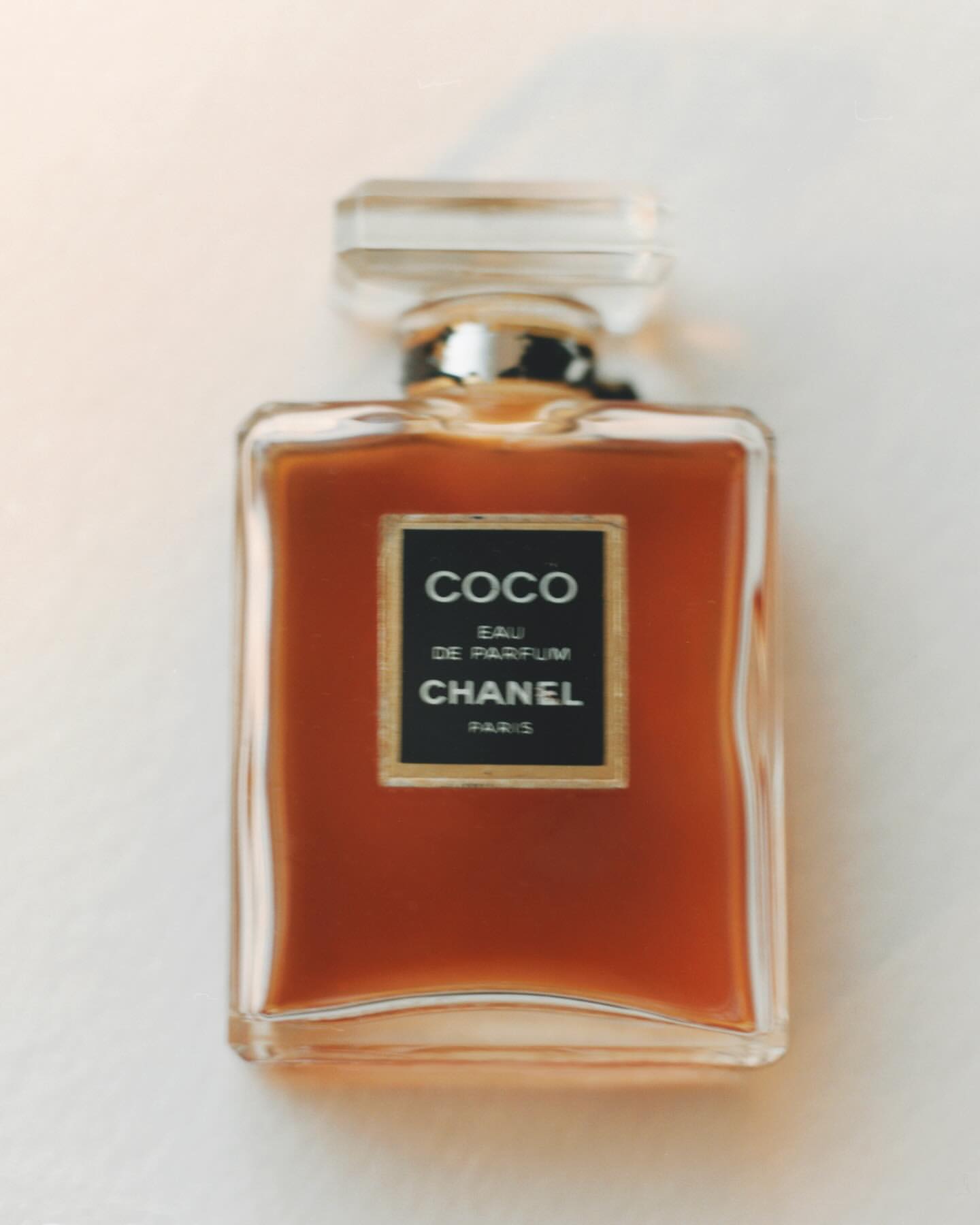 Chanel Coco Eau de Parfum bottle on a white surface. The perfume has a square shape, clear cap, and is filled with amber liquid.